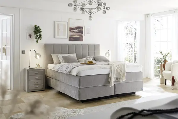 Modernes Schlafzimmer mit grauem Boxspringbett, gepolstertem Kopfteil, Nachttischen und weichen Textilien – hochwertiges Bett für erholsamen Schlaf, elegantes Schlafzimmerdesign, Komfortbett in Grau, skandinavischer Wohnstil.